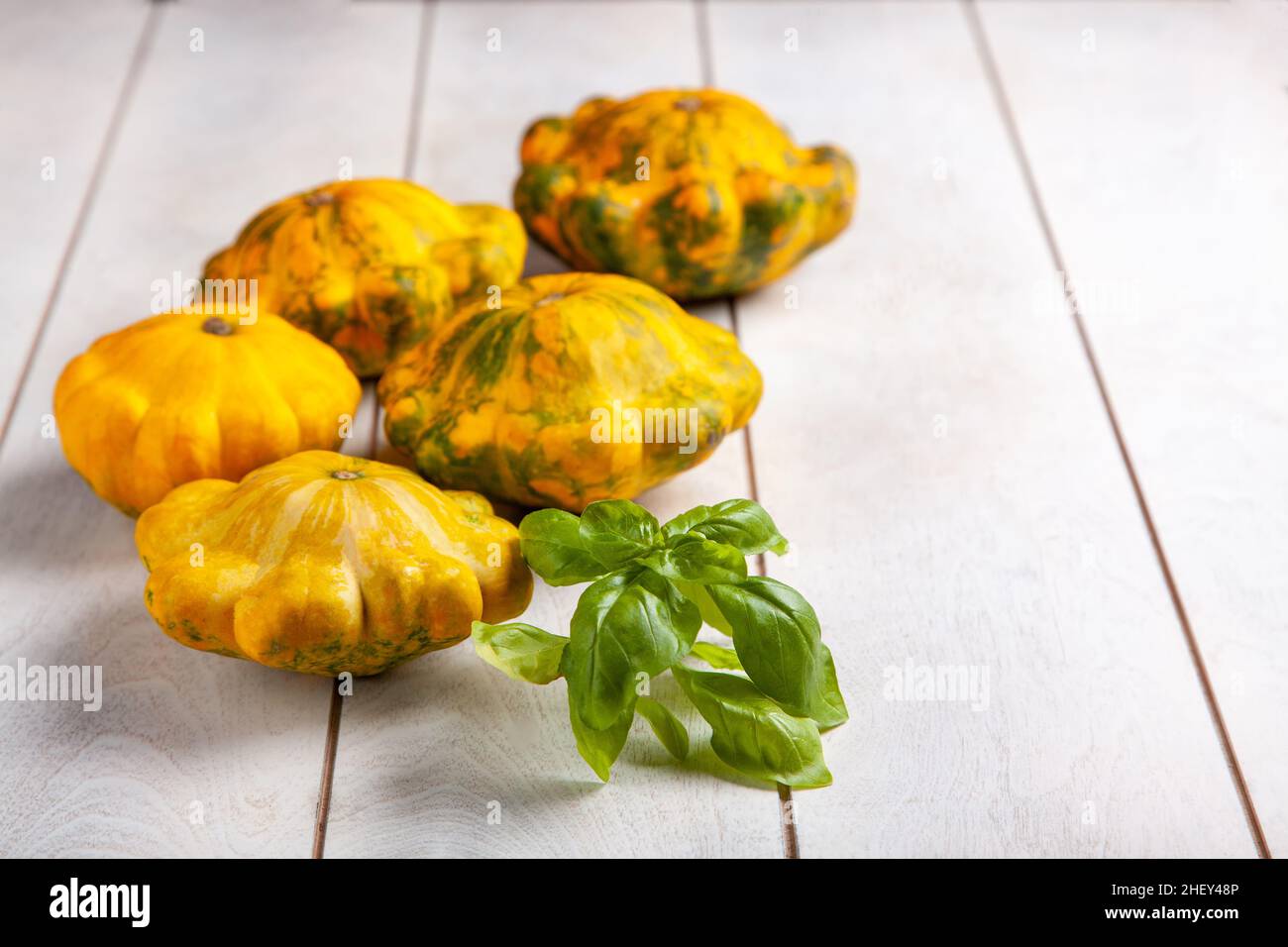 Gelbe patissons oder Kürbis und ein Basilikumblatt auf hellem Holzgrund. Stockfoto