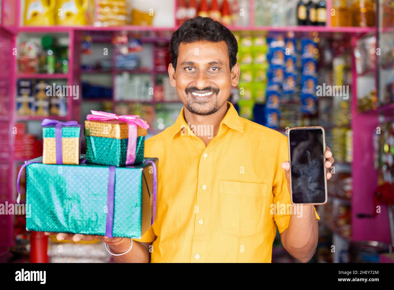 Kirana Shop Händler mit Geschenkboxen und Handy in der Hand, die an der Kamera - concpet von Festival-Verkäufe, Werbeangebote, um Preise zu gewinnen Stockfoto