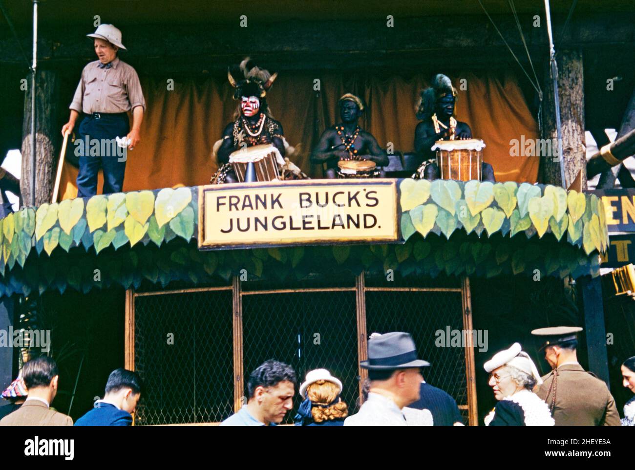 ‘Native’ Trommler und ein barker am Eingang zu ‘Frank Buck’s Jungleland’ auf der New Yorker Weltausstellung 1939. Zu dieser Unterhaltung gehörten Tausende von seltenen Exemplaren von Vögeln, Reptilien und wilden Tieren sowie Elefanten und Kamelritte. Texan Frank Buck (1884–1950) wanderte in den Dschungel der Welt, um wilde Tiere, Vögel und Reptilien für die amerikanischen Zoos und Zirkusse zu sammeln – er war bekannt als Frank ‘Bring 'em Back Alive' Buck. Bis Ende des Jahres 1920s war Buck der weltweit führende Anbieter von Wildtieren. Dieses Bild stammt von einem alten Kodak Amateur aus dem Jahr 1930s. Stockfoto