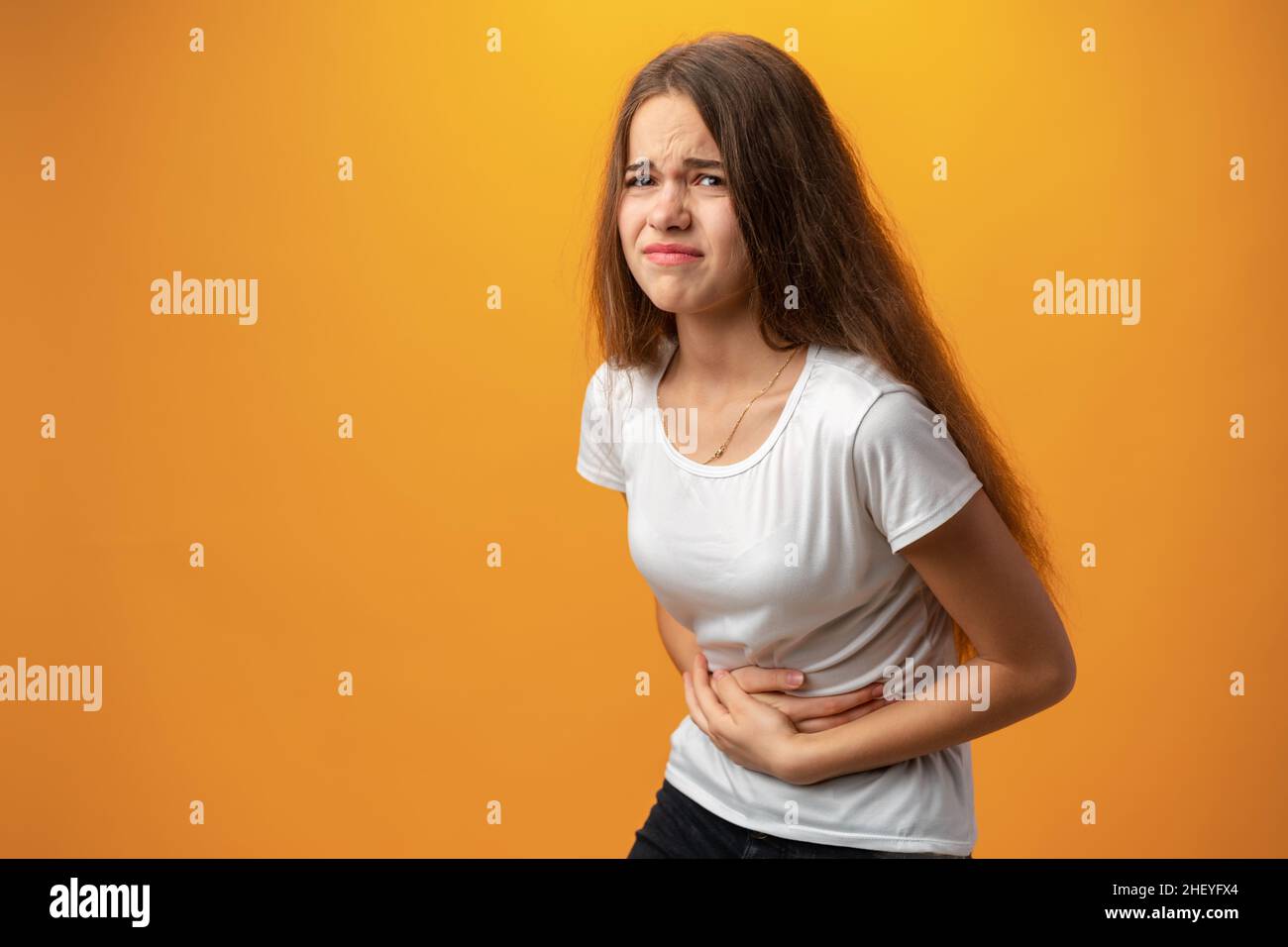 Teenagermädchen mit Bauchschmerzen vor gelbem Hintergrund Stockfoto
