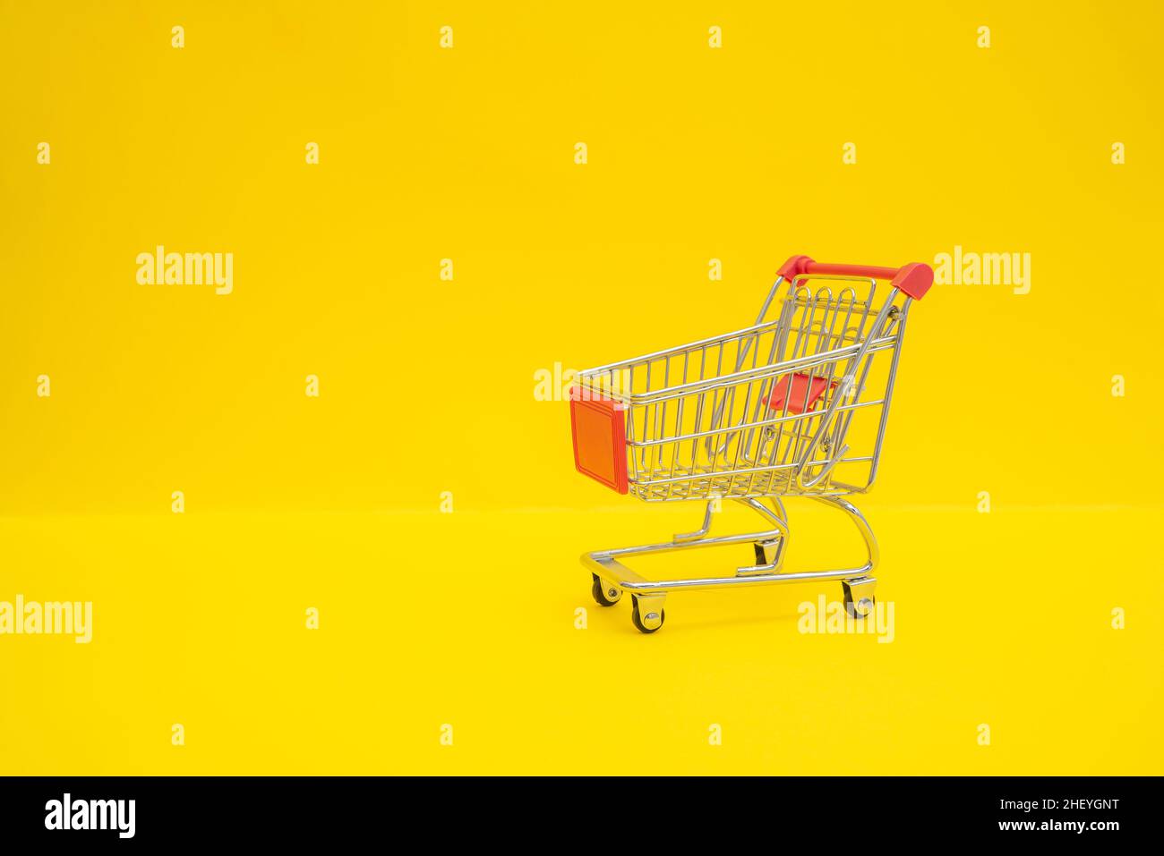 Kleiner Einkaufswagen aus Stahl auf gelber Oberfläche Stockfoto