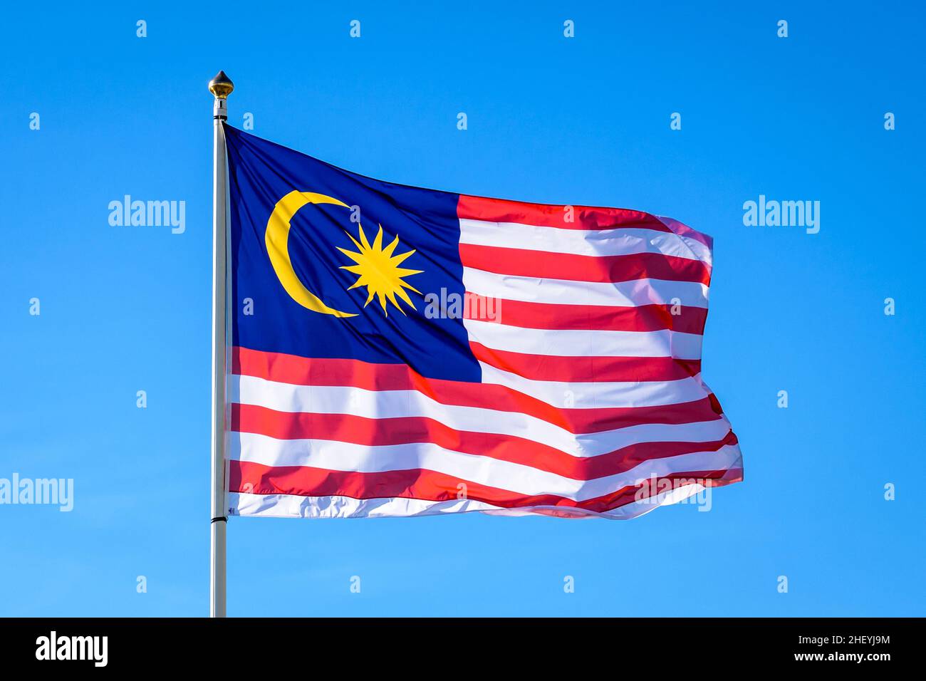 Die Nationalflagge Malaysias fliegt im Wind mit vollem Mast gegen den blauen Himmel. Stockfoto