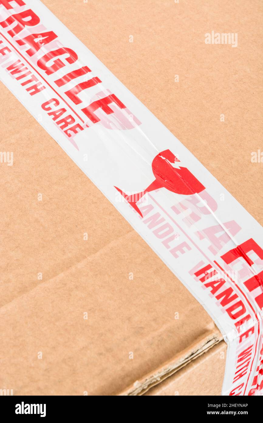 Versandkarton aus braunem Karton mit rot-weißem Haftklebeband aus Polypropylen, „Fragile Handle with Care“. Für etwas Fragiles. Stockfoto