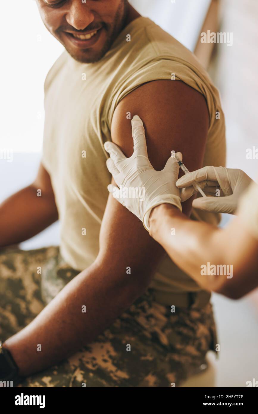 Junger Soldat, der eine Dosis des Covid-19-Impfstoffs in seinem Arm erhielt. Amerikanischer Militärangehöriger lächelt fröhlich, während er gegen Coronavirus di geimpft wird Stockfoto