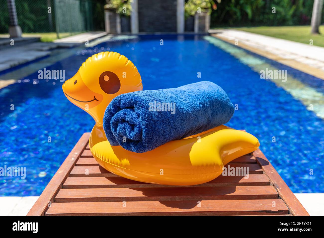 Gelbe, aufblasbare Ente mit einem blau gerollten Handtuch an der Seite des Schwimmbades. Urlaub, Sommerurlaub. Stockfoto