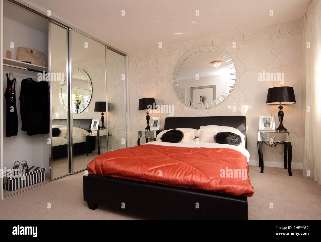 Schlafzimmer im modernen Showhome, Doppelbett mit Kingsize-Bett, orangefarbene Steppdecke, Bettdecke, Nachttischlampen, Wandtapete, verspiegelte Kleiderschränke Stockfoto