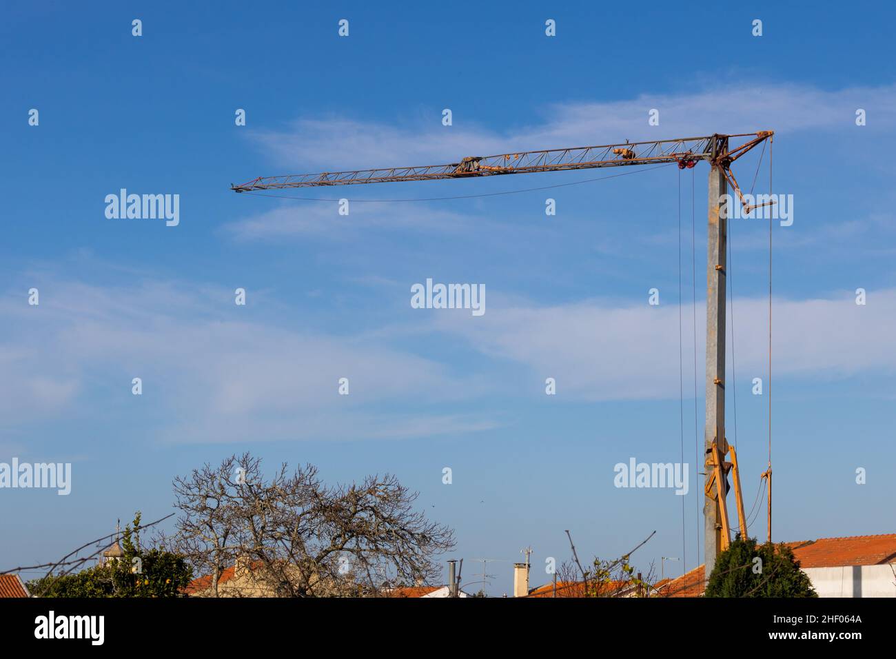 Ein Turmdrehkran, der auf einer Baustelle über den Dächern kleiner Wohnhäuser auf dem Land aufgestellt wurde, und ein blauer Himmel im Hintergrund Stockfoto