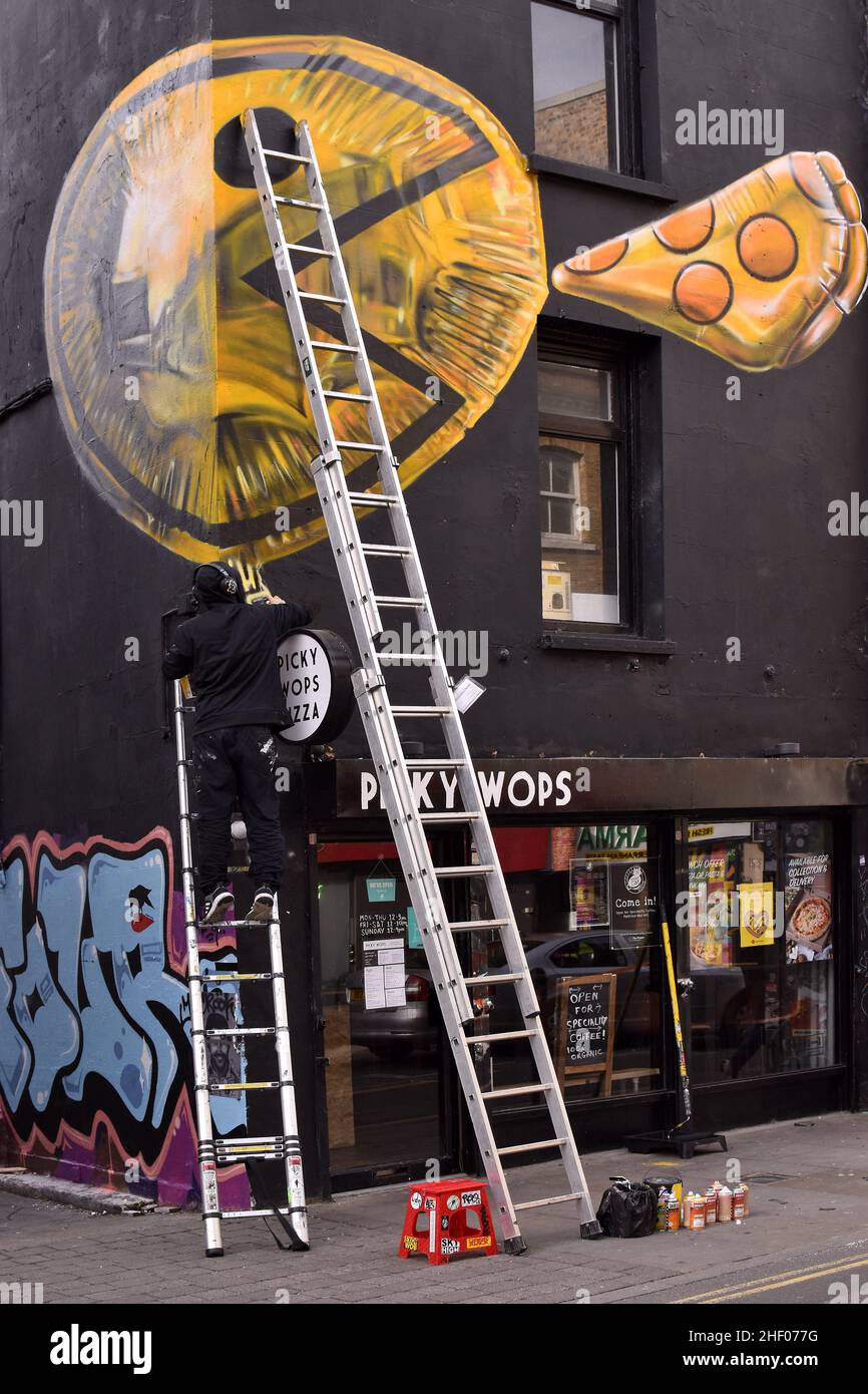Mann malte Kunstwerke an der Fassade der pingeligen Wops Pizzeria, Brick Lane im Osten Londons in Großbritannien. Stockfoto