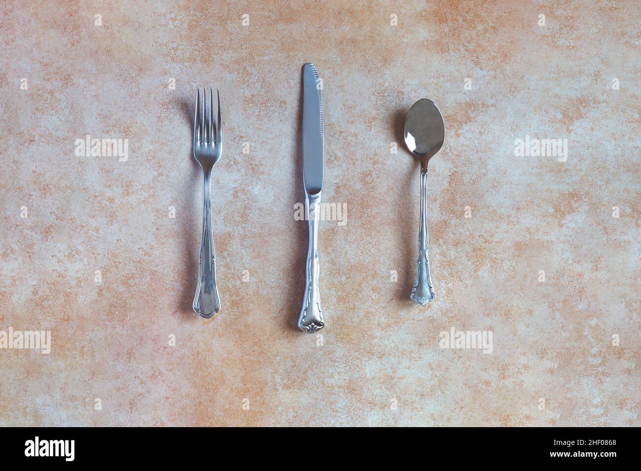 Ansicht eines antiken Silberbesteck, bestehend aus Gabel, Löffel und Messer, auf einem abstrakten Hintergrund und einer keramischen Textur in Pastellfarben. Ant Stockfoto