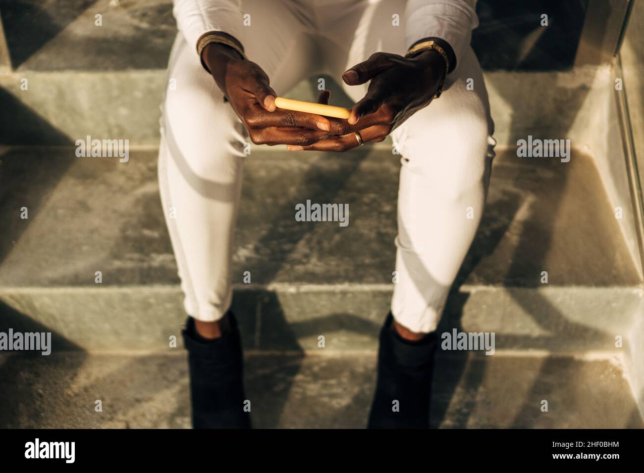 Nahaufnahme einer Frau, die ein Mobiltelefon benutzt, während sie auf einer Treppe sitzt. Stockfoto