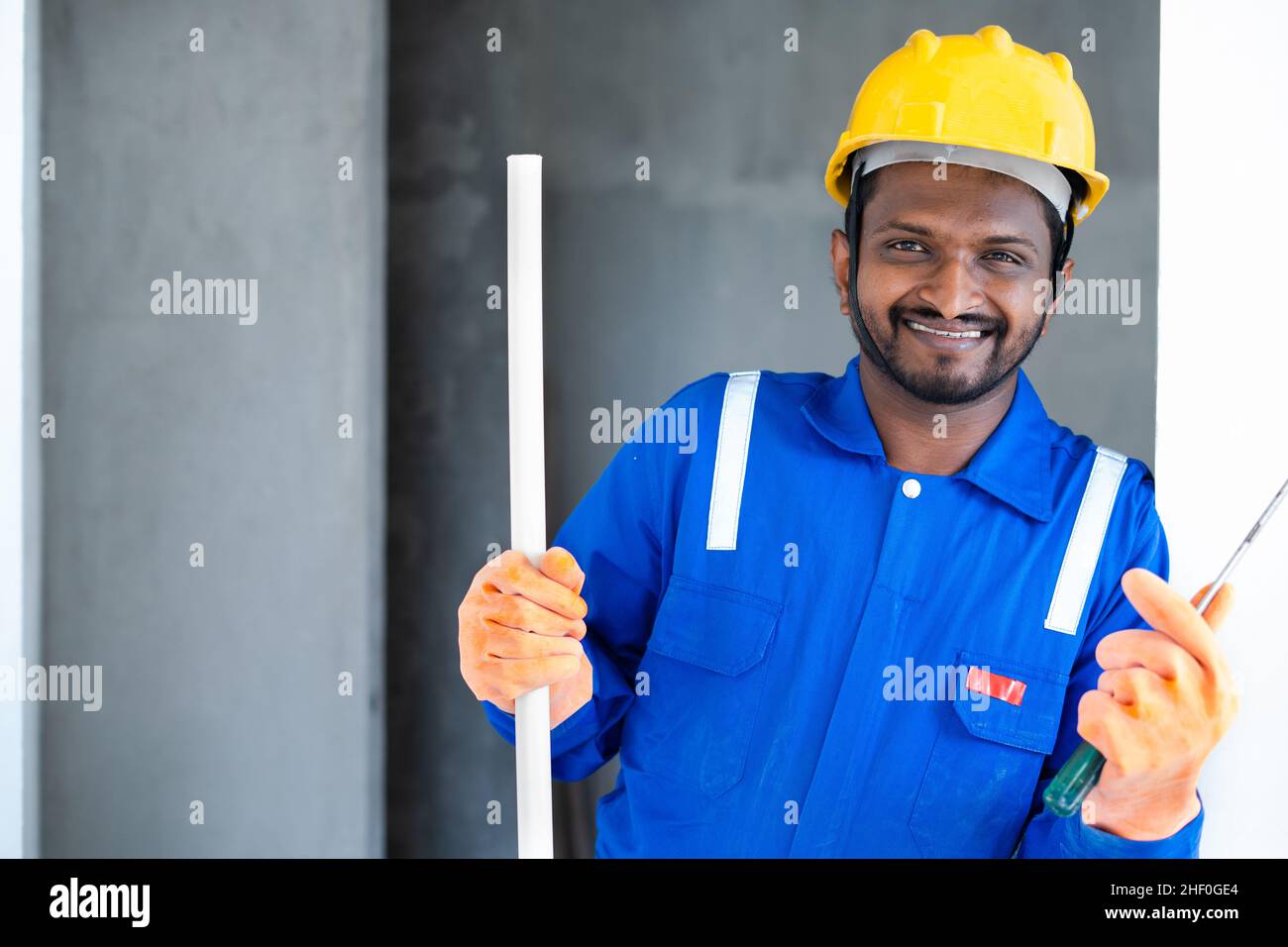 Lächelnder Klempner mit Rohr und Sanitär-Werkzeug in der Hand zeigt Daumen durch Blick auf die Kamera - Konzept des Servicemannes bereit zu arbeiten, Vertrauen und Stockfoto