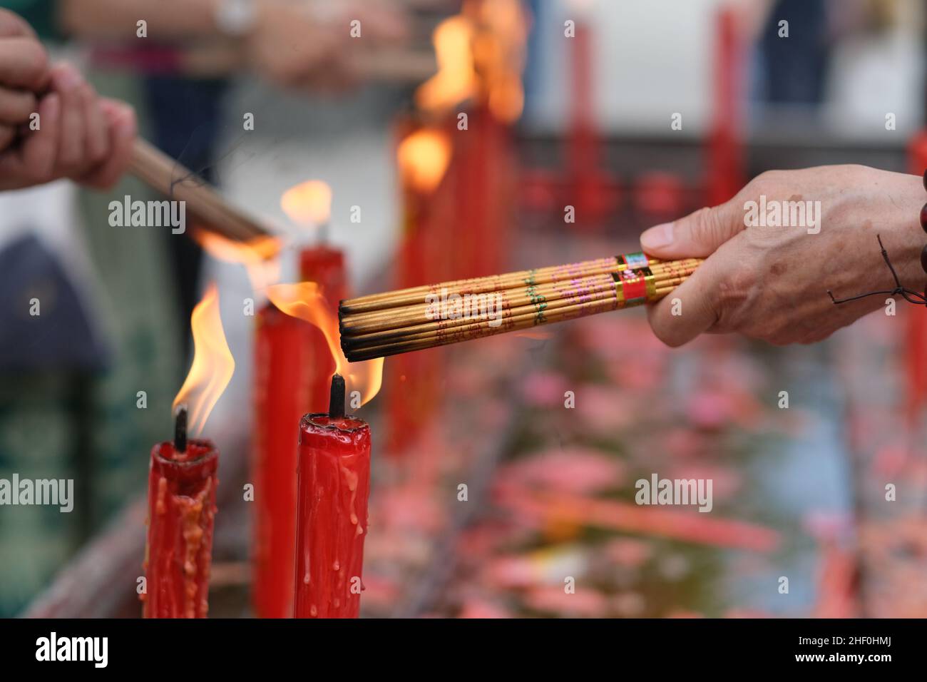 Nahaufnahme von Hand, die Räucherstäbchen auf dem Feuer der roten Kerze im Tempel verbrennt. Konzept der asiatischen Buddhismus-Kultur Stockfoto