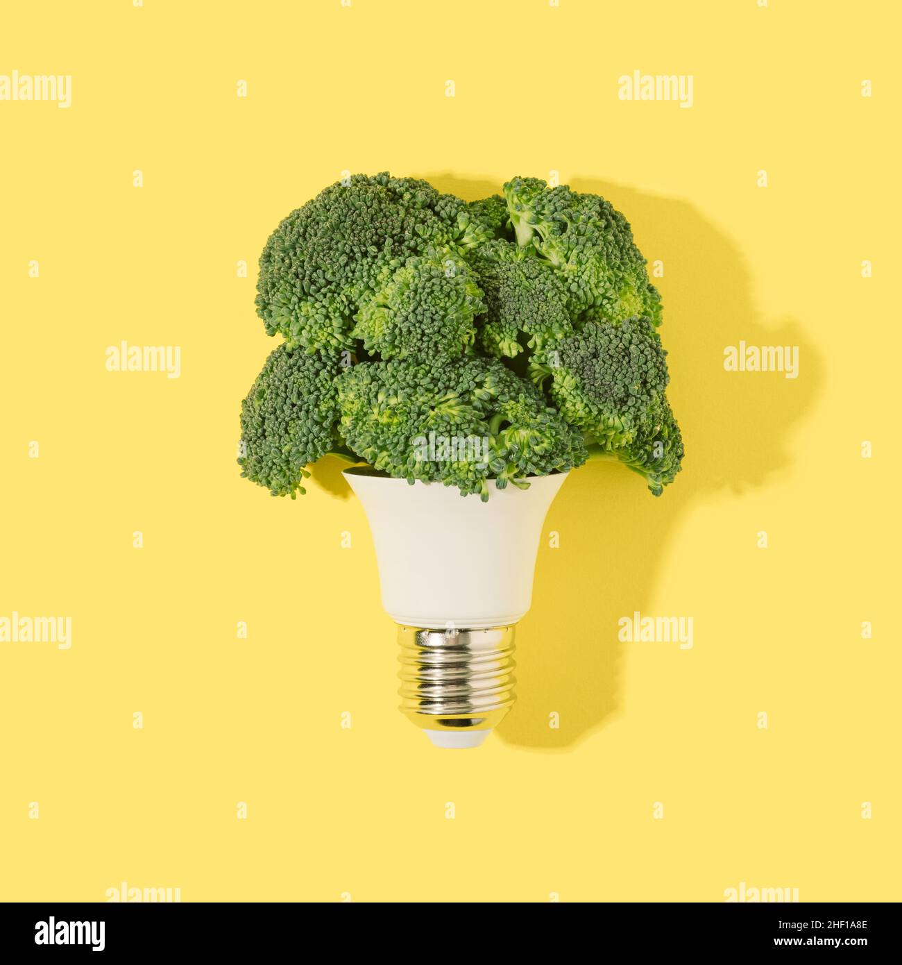 Glühbirne mit grünen Brokkoli-Blüten auf einem stark gelben Hintergrund. Erneuerbare Stromerzeugung Minimales Konzept. Stockfoto