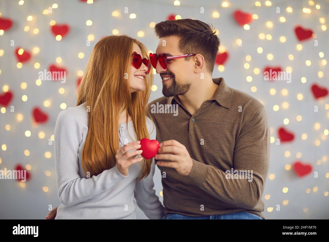Das Paar schaut sich sanft in die Augen und lehnt sich mit einem kleinen roten Herzen gegeneinander an Stockfoto