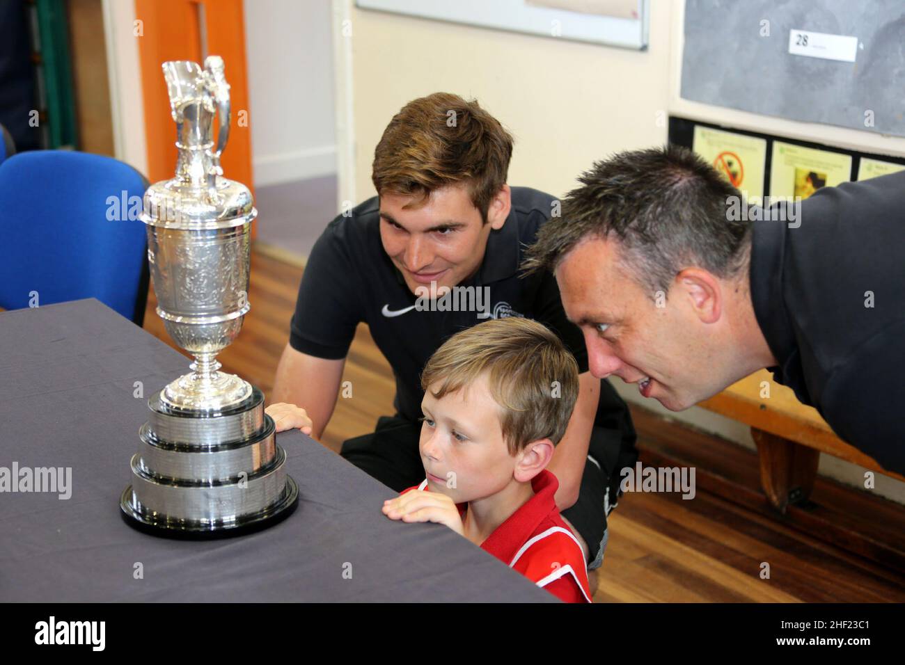 Ayrshire, Schottland, Großbritannien. Im Rahmen des Vorlaufs der Royal & Ancient Golf Club Open Championship 2015, die im Royal Troon Golf Club, Troon Ayrshire, stattfand. Die drei großen Trophäen der Claret Jug, die Amateur Championship, die Senioren Claret Jug ging um Grundschulen in Ayrshire, wo Schüler die Trophäen sehen und polieren durften. Mitarbeiter von PE und ein Schüler der Muirhead Primary School, Troon bewundern den Claret Krug Stockfoto