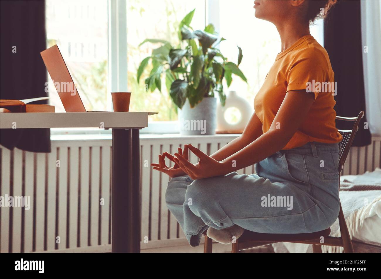 Stressabbau bei freiberuflicher Arbeit. Zugeschnittenes Foto einer afroamerikanischen Freiberuflerin, die in Lotushaltung sitzt und mit den Händen in Mudra gestu meditiert Stockfoto