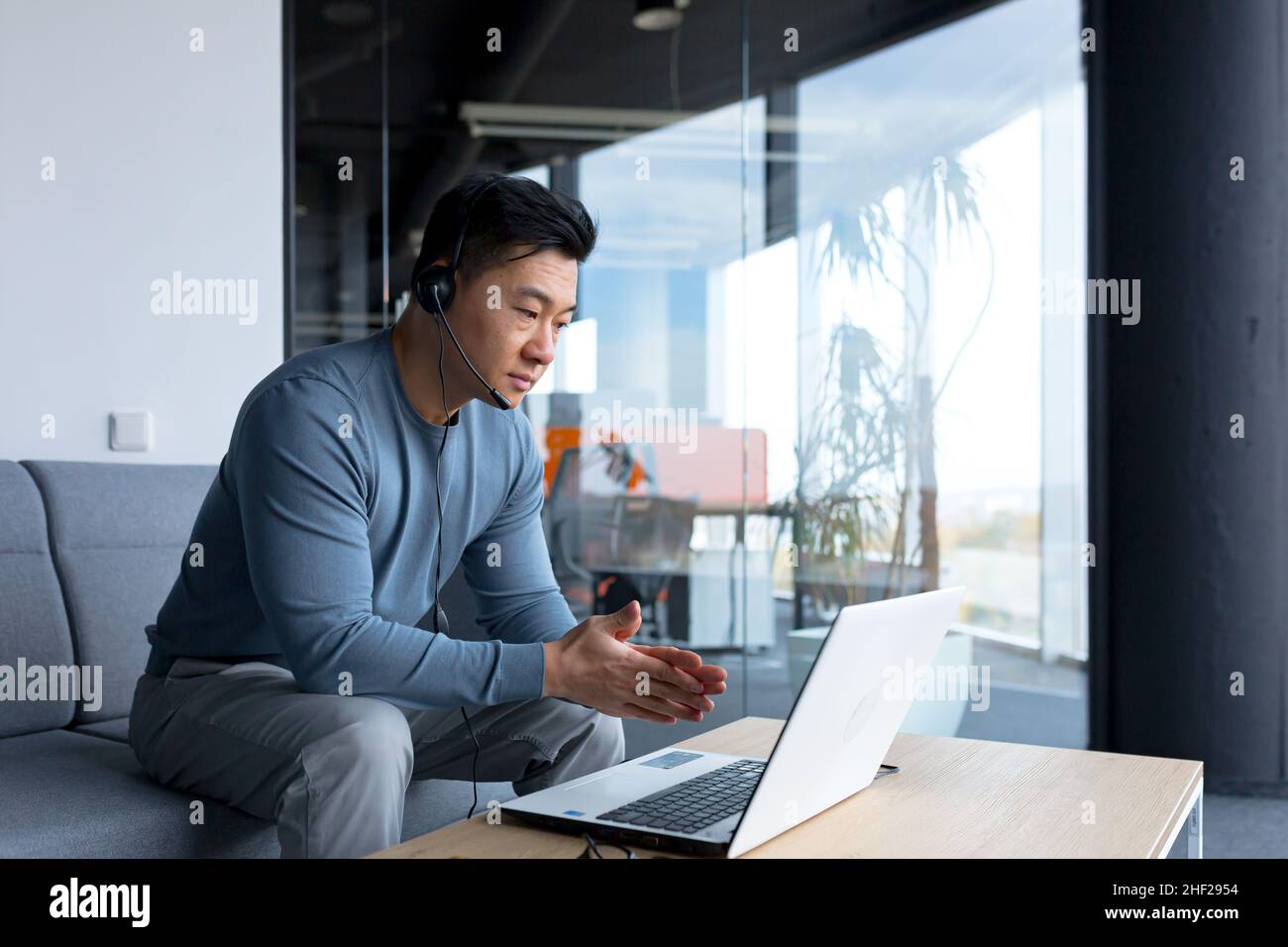 Porträt eines asiatischen Callcenter-Mitarbeiters, eines Mannes, der mit Headset und Computer arbeitet, einer Telearbeit, eines Videoanrufs, einer Online-Hilfe Stockfoto