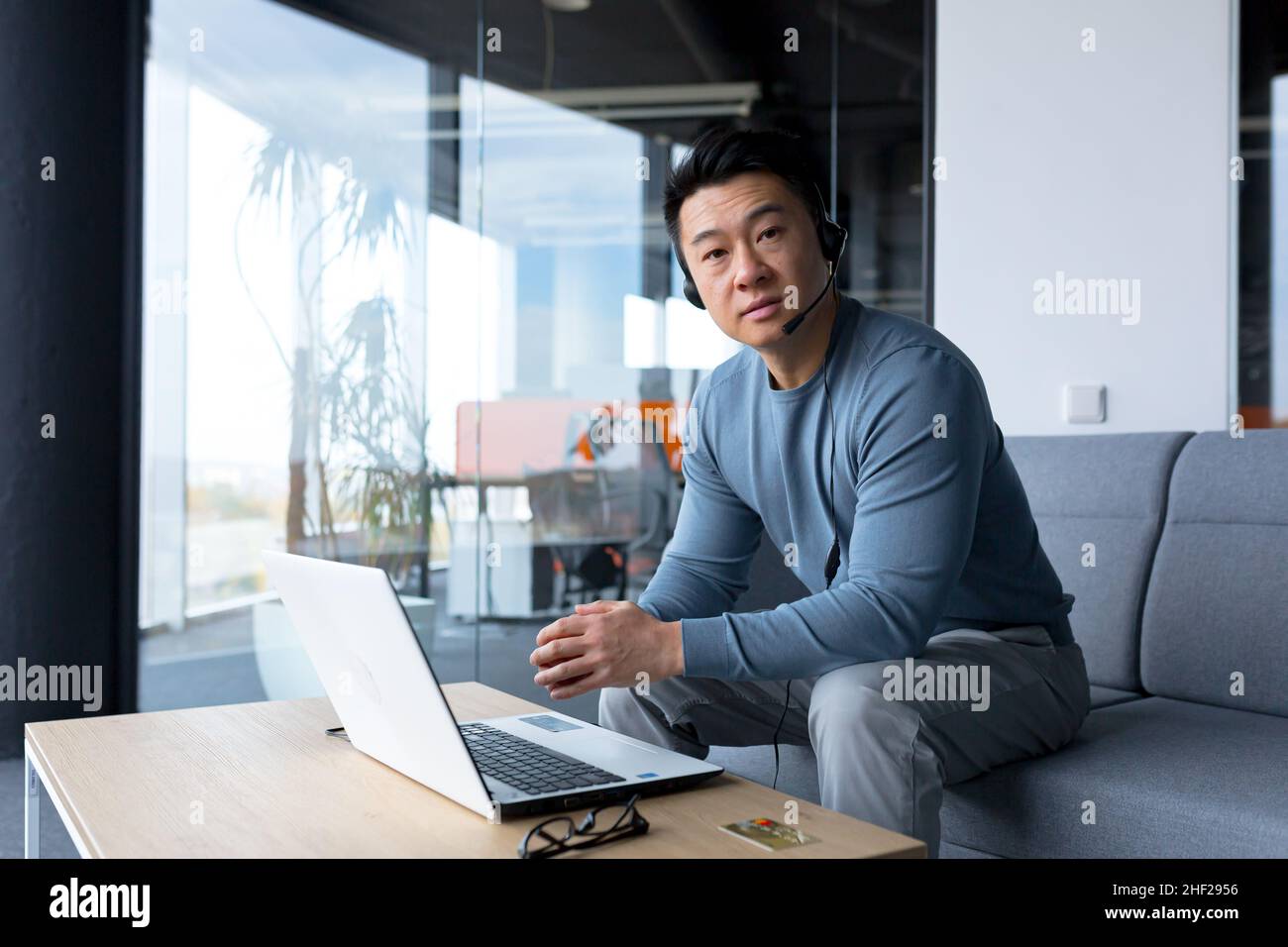 Porträt eines asiatischen Callcenter-Mitarbeiters, eines Mannes, der mit Headset und Computer arbeitet, einer Telearbeit, eines Videoanrufs, einer Online-Hilfe Stockfoto