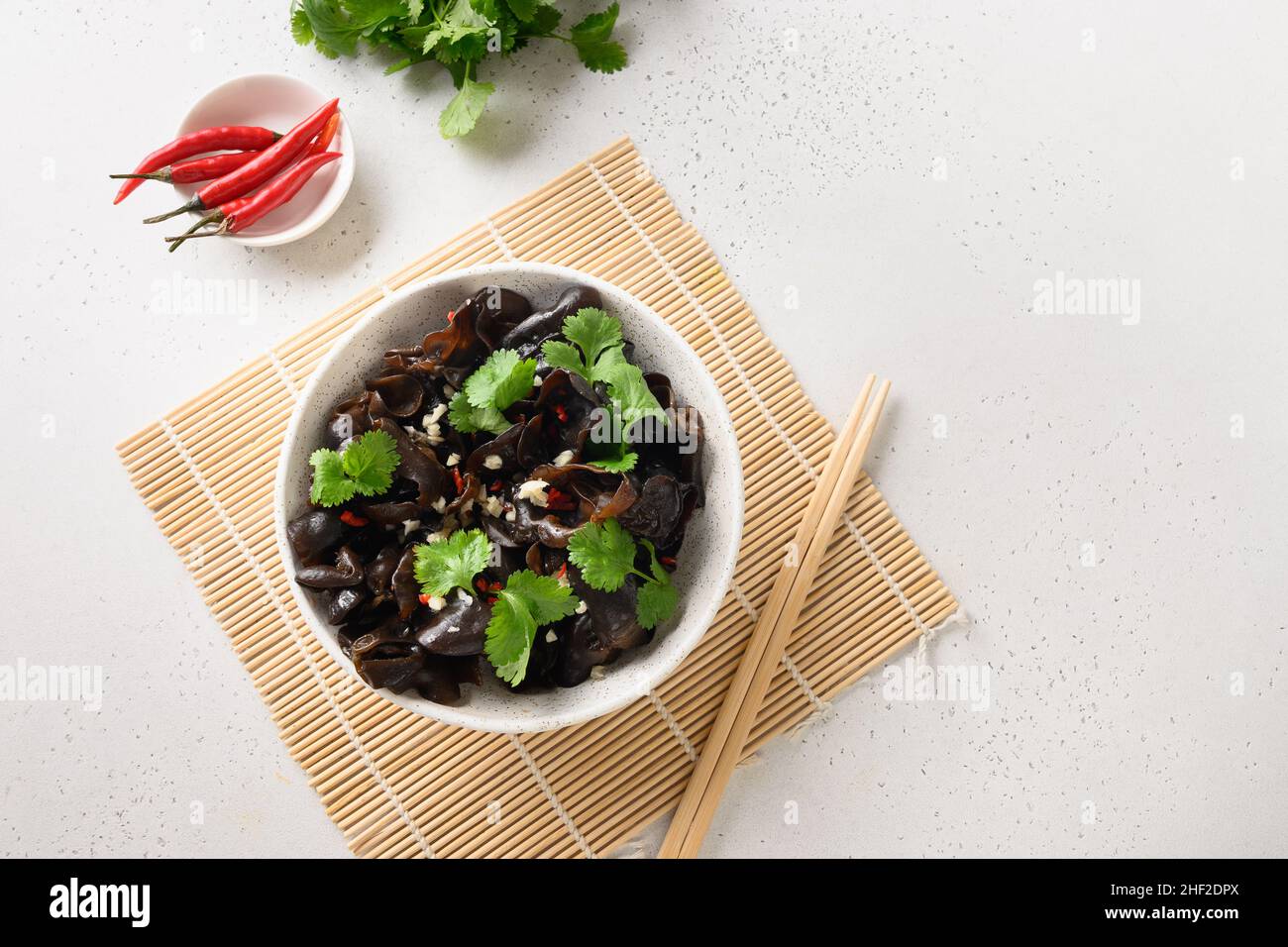 Chinesische Ähren-Schwarzmühlenpilze mit Chilli und Koriander auf weißem Hintergrund. Blick von oben. Stockfoto