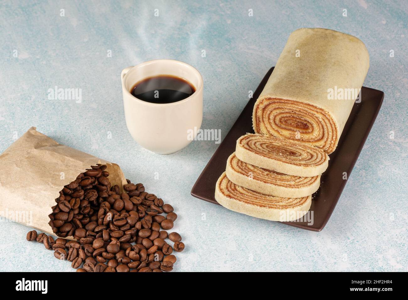 In Scheiben geschnittener Bolo de rolo (Rollkuchen) neben Bohnen und Kaffeetasse. Stockfoto
