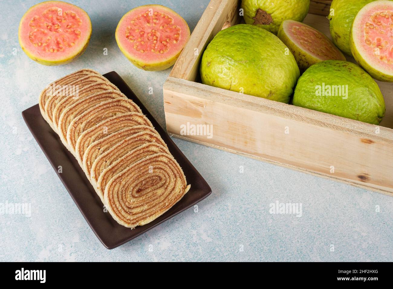 In Scheiben geschnittener Bolo de rolo (Rollkuchen) neben einer Schachtel mit Guavas. Stockfoto