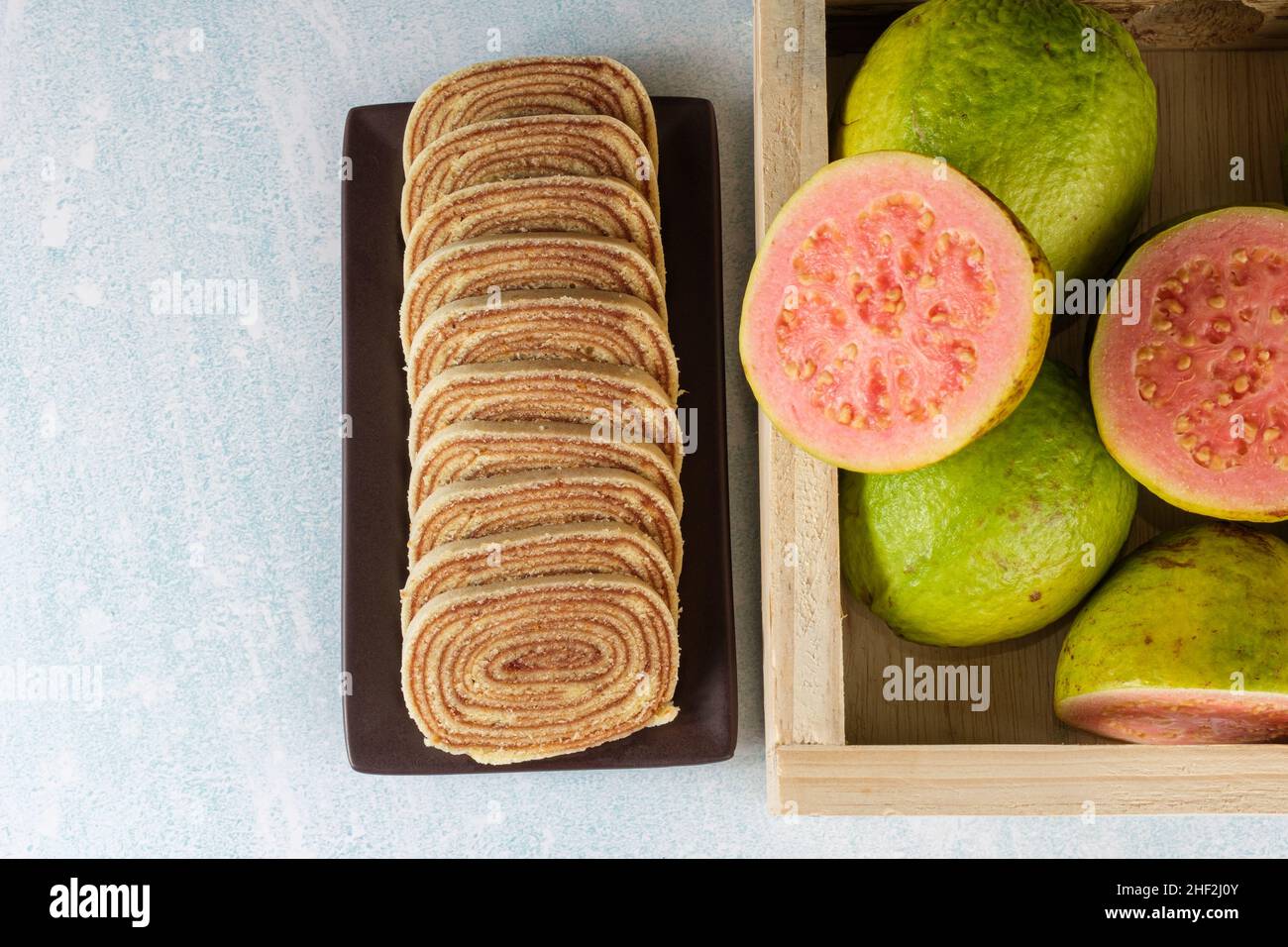 Geschnittenes bolo de rolo neben einer Schachtel mit Guavas (Space Copy). Stockfoto