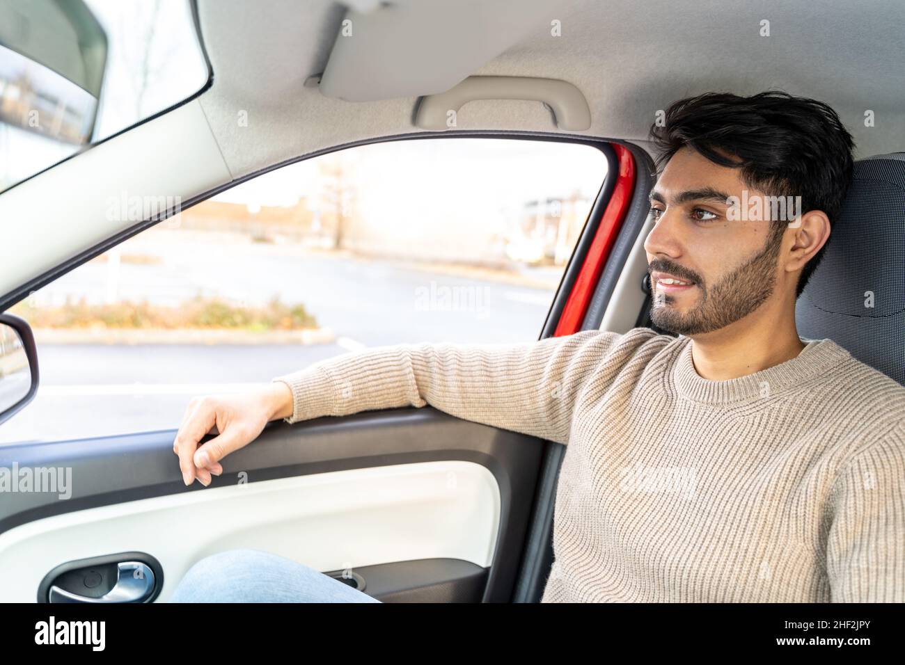 Mann im Pullover sitzt auf dem Beifahrersitz und fährt tagsüber im Auto Stockfoto