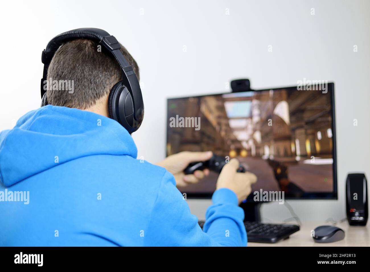 Mann in Kopfhörern spielt mit einem Gamepad ein Computerspiel auf einem Desktop-PC. Konzept der Spielsucht, Freizeit zu Hause Stockfoto