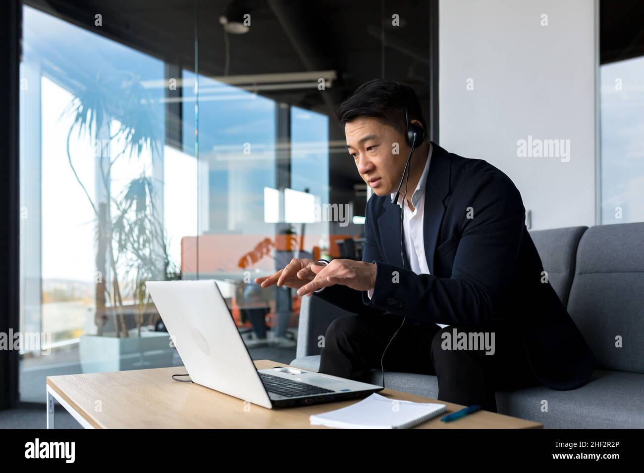 Ein Mitarbeiter im asiatischen Callcenter spricht mit Kunden im Büro, ein asiatischer Geschäftsmann nutzt ein Headset und einen Laptop für einen glücklichen und lächelnden Videoanruf Stockfoto