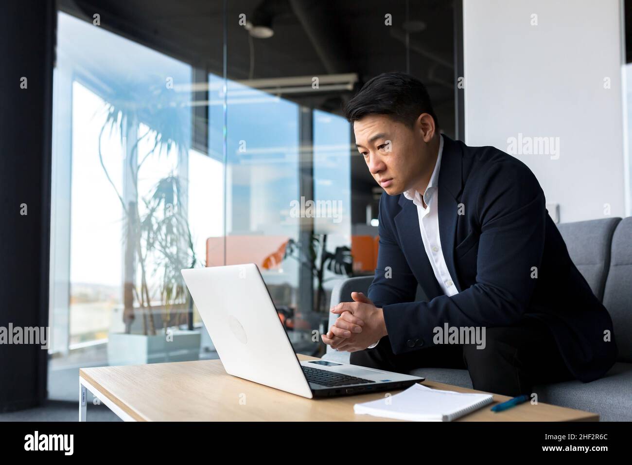 Asiatisch nachdenklicher Geschäftsmann bei Laptop, denken über die Schaffung einer neuen Geschäftsstrategie, erfolgreicher Mann, der im Büro am Laptop arbeitet Stockfoto