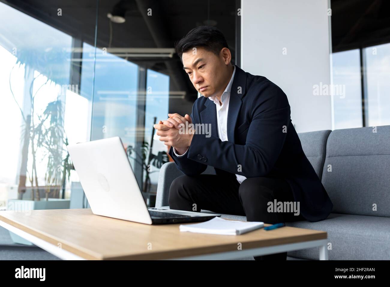 Asiatisch nachdenklicher Geschäftsmann bei Laptop, denken über die Schaffung einer neuen Geschäftsstrategie, erfolgreicher Mann, der im Büro am Laptop arbeitet Stockfoto
