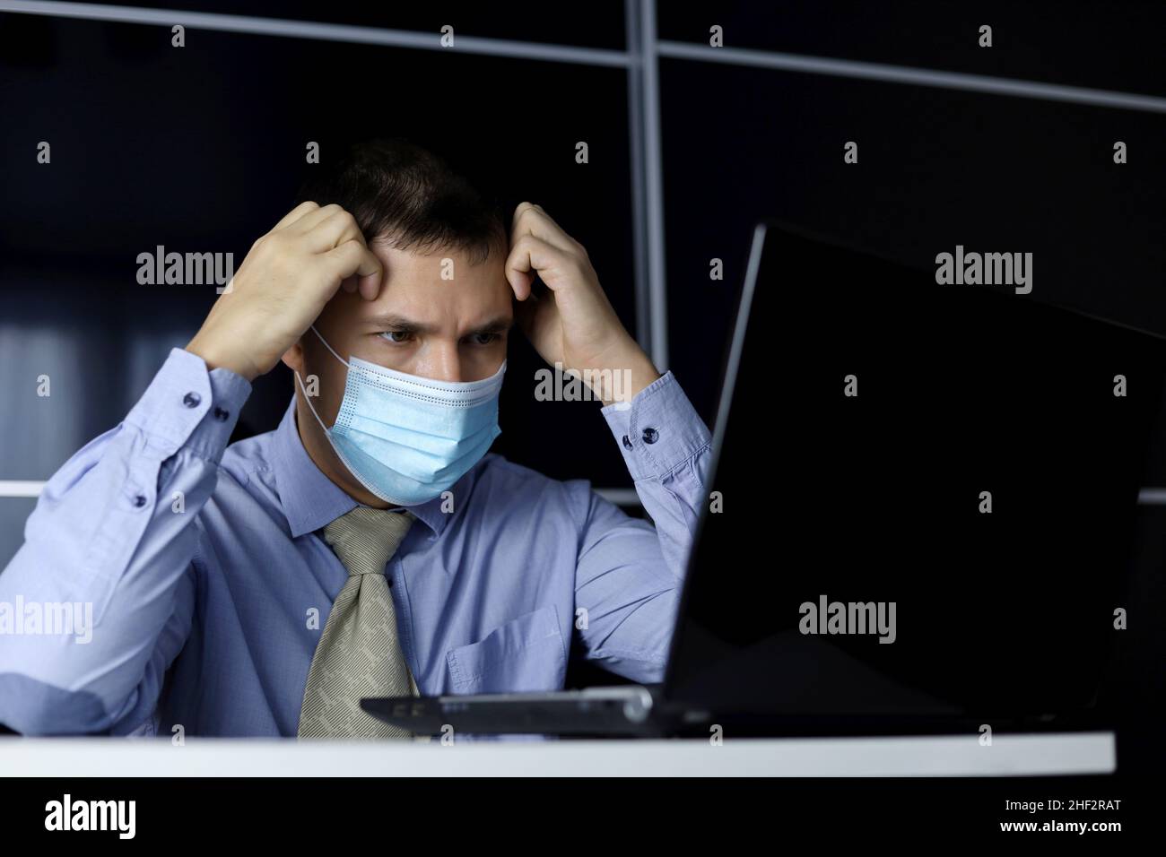 Mann in Gesichtsmaske und Bürokleidung, der auf das Notebook-Display aufgeregt aussicht. Konzept zur Lösung einer schwierigen Aufgabe, eines kritischen Fehlers Stockfoto