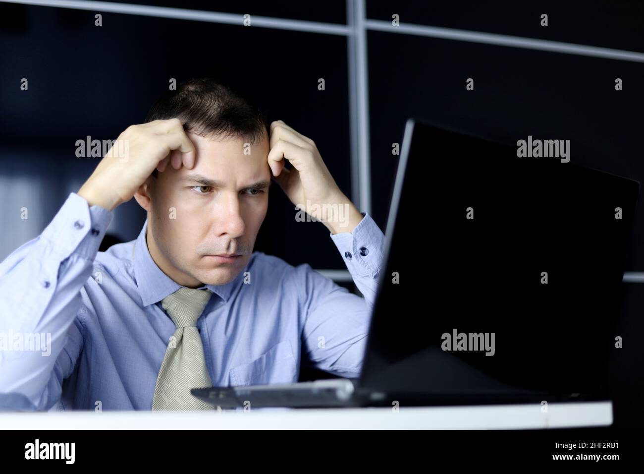 Mann in Bürokleidung, der aufgeregt auf den Laptop-Bildschirm schaut. Konzept der schwierigen Arbeitsaufgabe, schlechte Nachrichten, langweilige Arbeit oder Kopfschmerzen Stockfoto