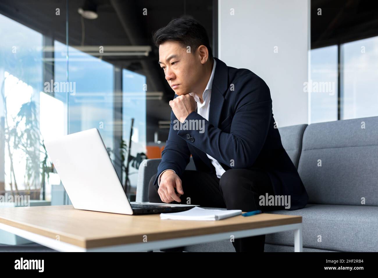 Asiatisch nachdenklicher Geschäftsmann bei Laptop, denken über die Schaffung einer neuen Geschäftsstrategie, erfolgreicher Mann, der im Büro am Laptop arbeitet Stockfoto