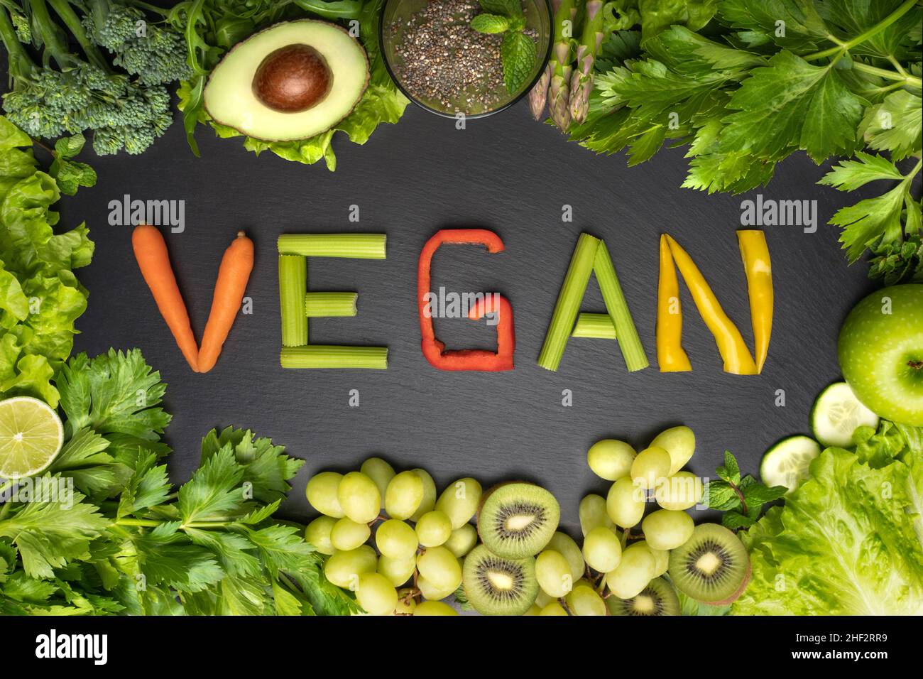 Draufsicht auf frisches grünes Gemüse und Obst Rahmen mit Wort vegan auf schwarzem Hintergrund. Veganes Essen und veganes Diät-Konzept Stockfoto