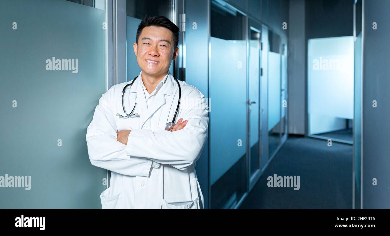 Porträt eines erfolgreichen glücklichen und fröhlichen asiatischen Arztes, Mann in einer modernen Klinik, der die Kamera anschaut und lächelt Stockfoto