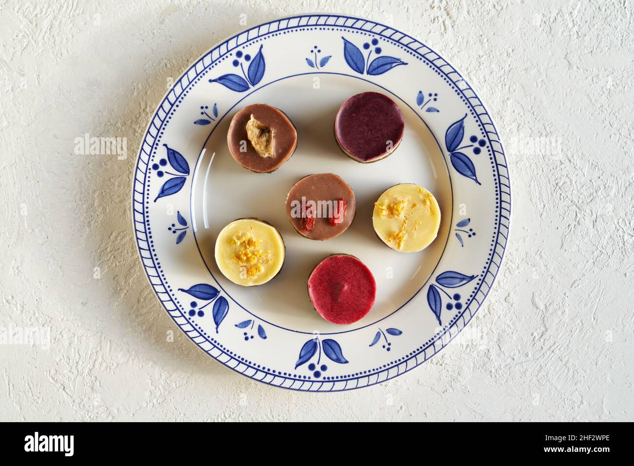 Vegane Mini-Desserts mit Heidelbeere, Goji, Himbeere, Zitrone und Banane auf einem dekorierten Teller auf weißem Hintergrund, Draufsicht Stockfoto