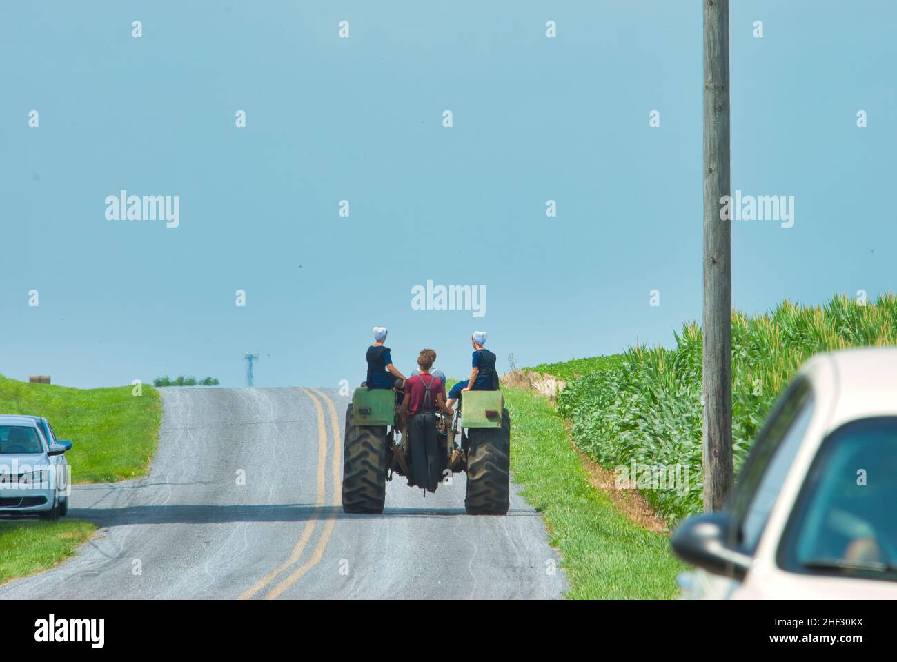Jugendliche mit Amish Boy und Girl, die an einem Sommertag auf einem alten Traktor auf einem Ackerland reiten Stockfoto
