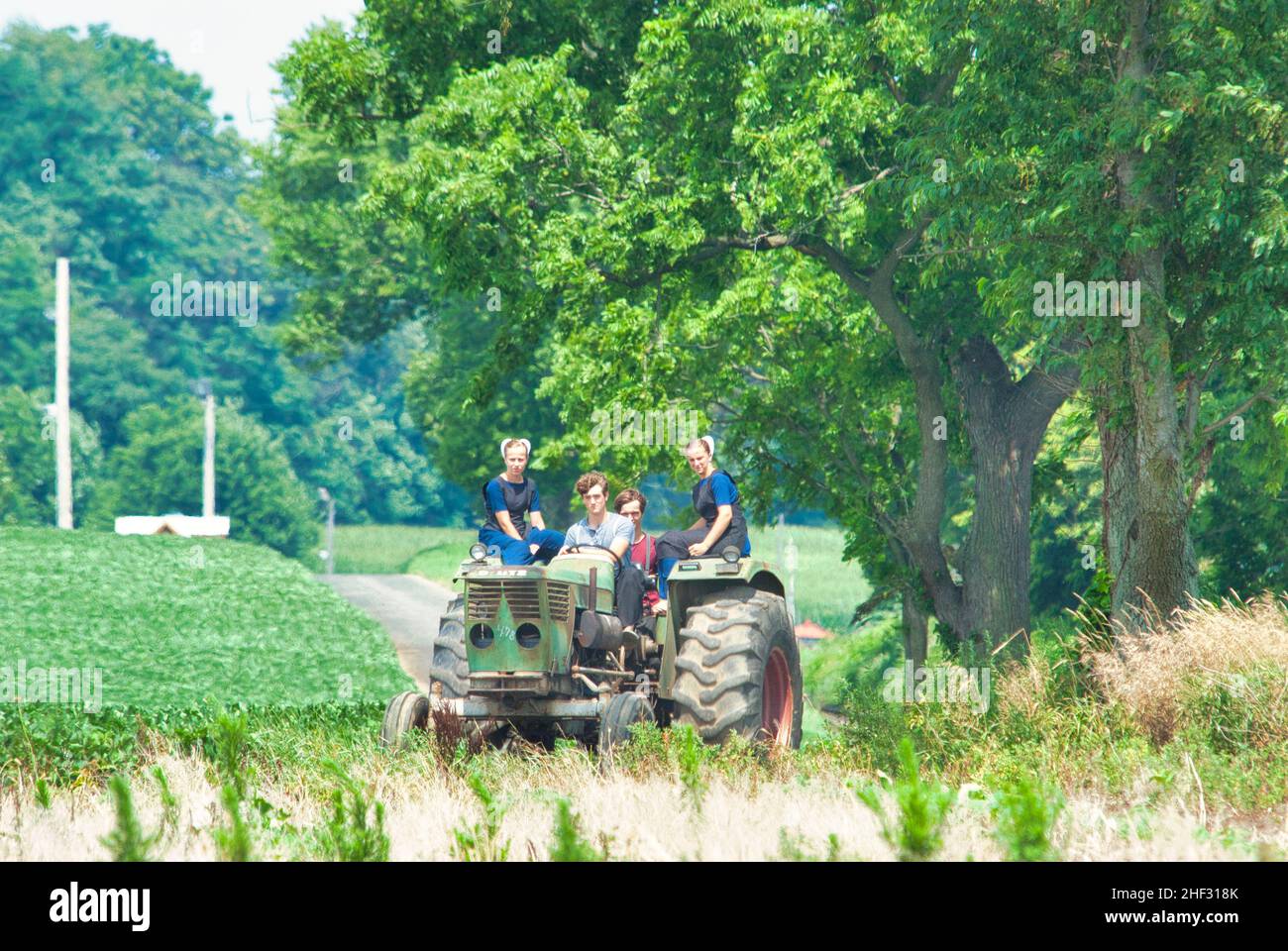 Ronks, Pennsylvania, Juli 2021 - Amish Boy und Girl Teenagers, die an einem Sommertag auf einem alten Traktor auf Ackerland reiten Stockfoto