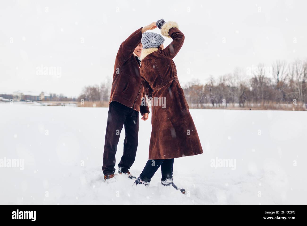 Ältere Familienpaare tanzen bei schneebedecktem Winterwetter im Freien. Ältere Menschen, die Spaß haben. Valentinstag Spaziergang Stockfoto