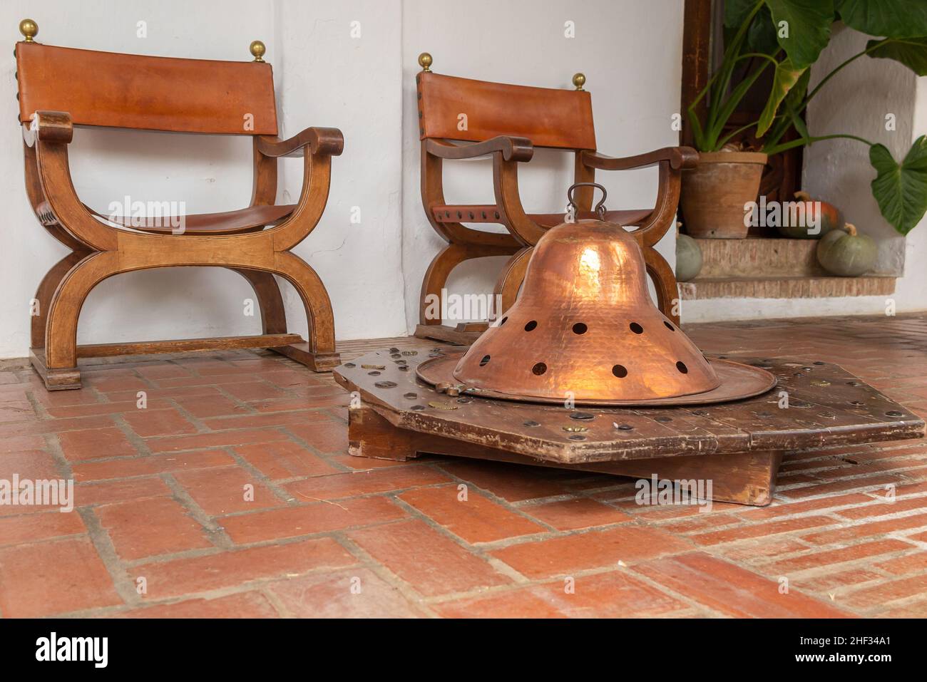 Innenhofszene mit einem antiken Tischbrazier auf einem Holzständer vor zwei antiken Holzstühlen.der Brazier wurde für viele genutzt Stockfoto