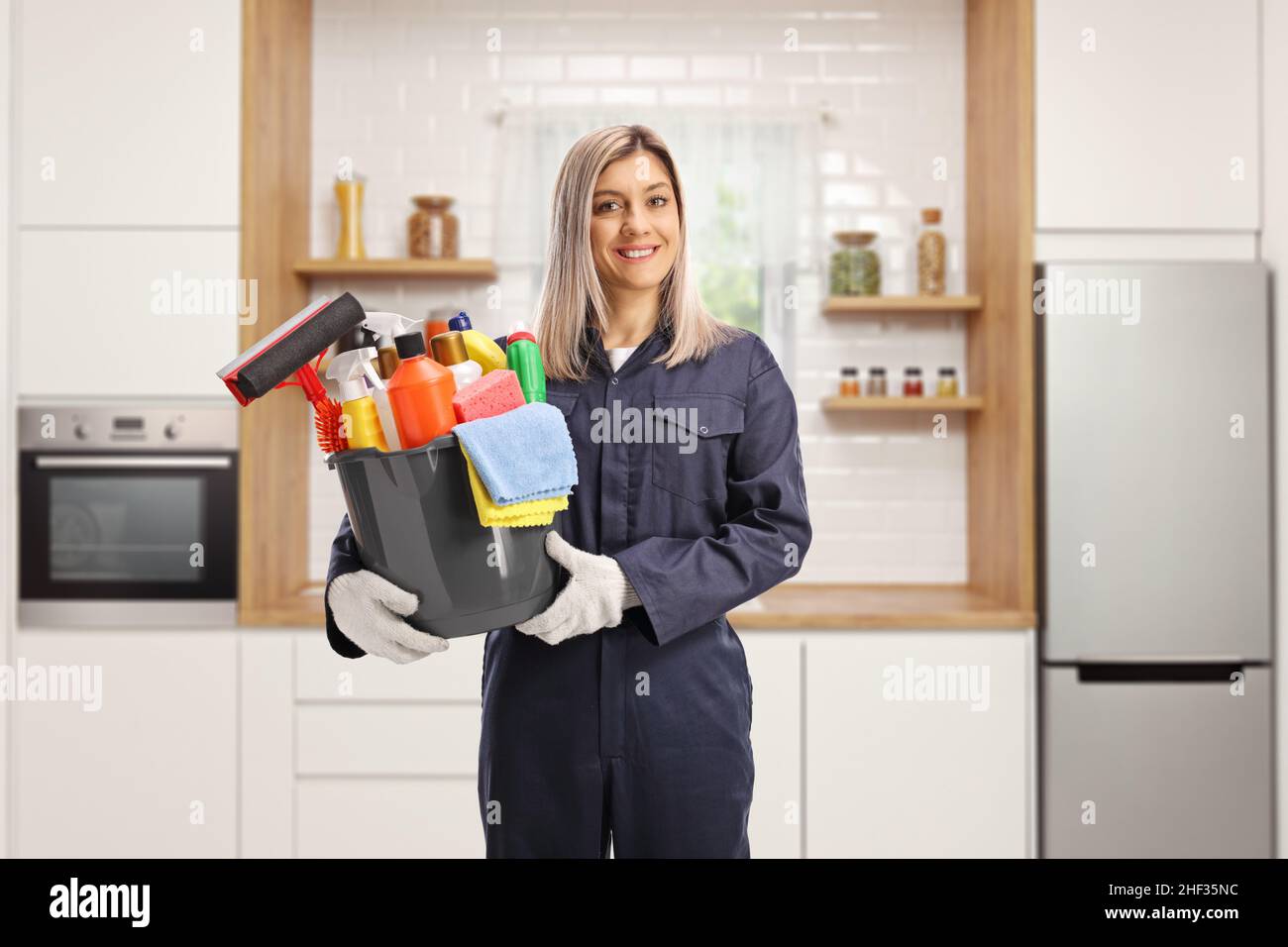 Professionelle weibliche Reinigungskraft in einer Uniform, die einen Eimer mit Reinigungsmitteln in einer Küche hält Stockfoto