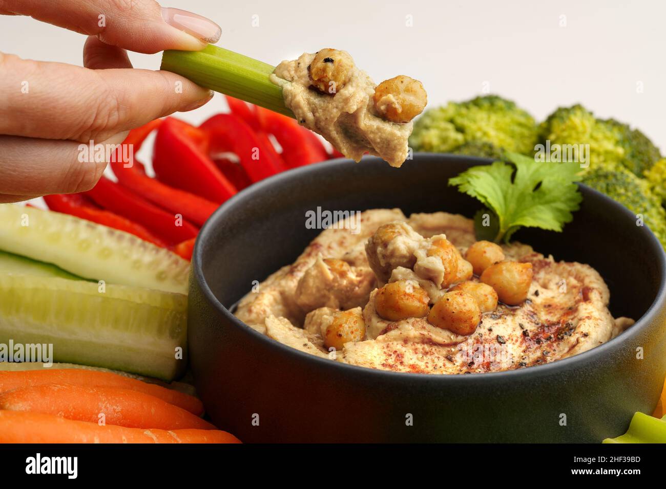 Nahaufnahme der Frau Hand hält Sellerie Stick mit Kichererbsen Hummus. Leckerer Hummus mit Gemüse und geräuchertem Paprika Stockfoto