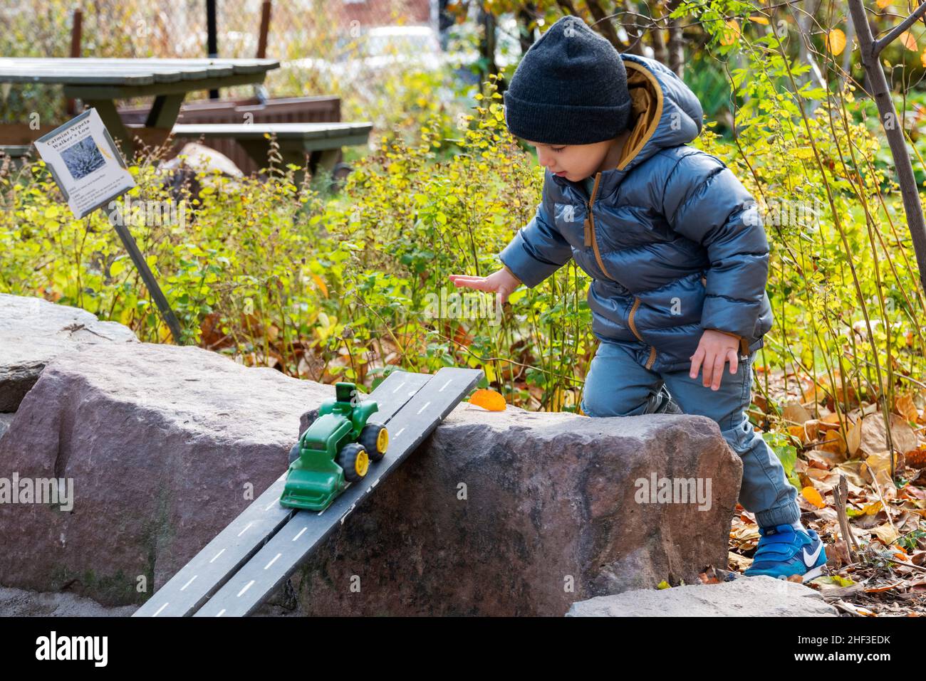 Zwei Jahre alter Junge, der mit einem Spielzeugschlepper auf einer Rampe im Sandkasten des Stadtparks spielt Stockfoto
