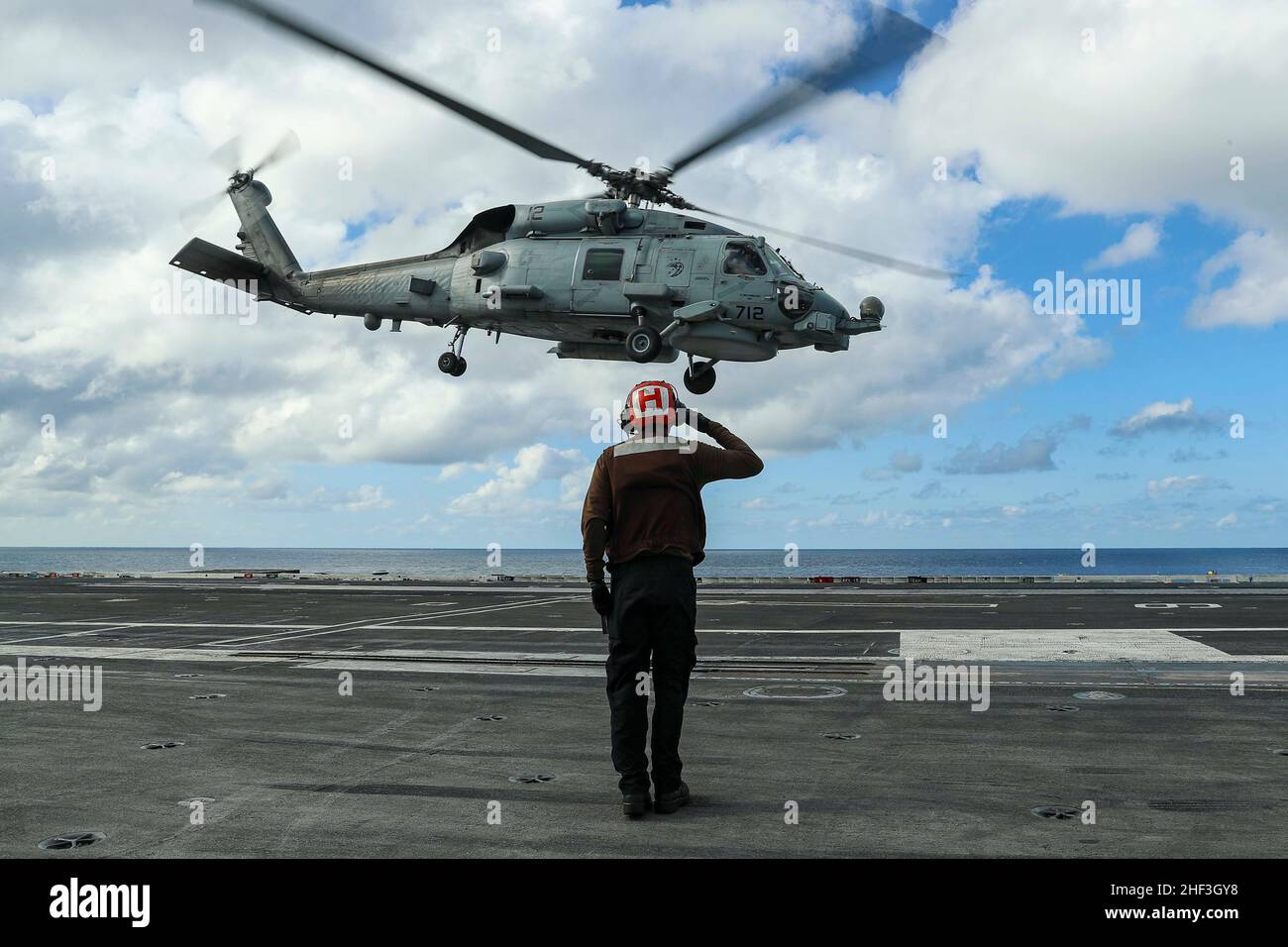 PAZIFISCHER OZEAN (Jan 11, 2022) die Mate 3rd-Klasse Erik Aguilar von Aviation Machinist aus Los Lunas, N.M., begrüßt einen MH-60R Sea Hawk-Hubschrauber, der den „Raptors“ von Helicopter Maritime Strike Squadron (HSM) 71 zugewiesen wurde, als er vom Flugdeck der USS Abraham Lincoln (CVN 72) abhebt. Die Abraham Lincoln Carrier Strike Group, angeführt von der Carrier Strike Group 3, wurde von San Diego, Januar 3, zur Unterstützung der globalen maritimen Sicherheitsoperationen eingesetzt. Als integraler Bestandteil der US-Pazifikflotte betreibt die US-3rd-Flotte Marinestreitkräfte im Indo-Pazifik und bietet die realistische, relevante Ausbildung, die für Fla erforderlich ist Stockfoto