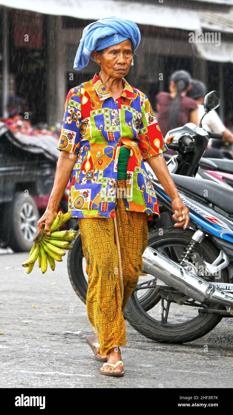 Eine ältere balinesische Frau mit einer bunten Bluse, die Bananen trägt, auf dem Sukawati-Markt in Bali, Indonesien Stockfoto