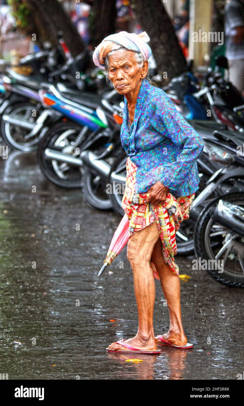 Eine alte, in Batik gekleidete balinesische Frau, die in einer Straße auf dem Sukawati-Markt in Bali, Indonesien, spaziert Stockfoto