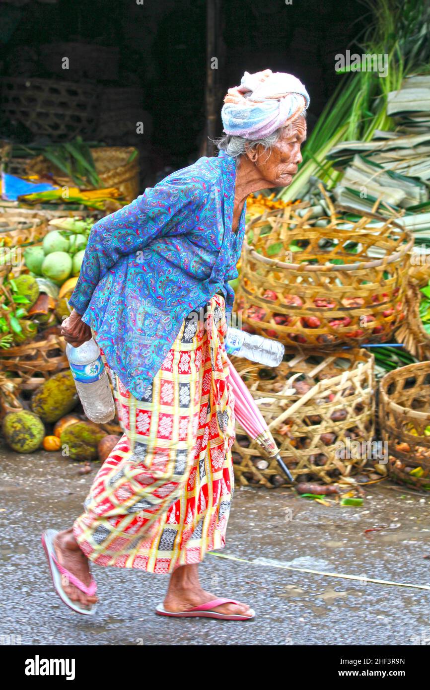 Eine alte, in Batik gekleidete balinesische Frau, die in einer Straße auf dem Sukawati-Markt in Bali, Indonesien, spaziert Stockfoto