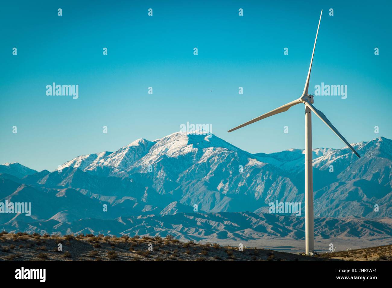 Windkraftanlage Turbine und San Bernardino Mountains bedeckt von Schnee, Kalifornien, USA. Thema „Grüne Energieversorgung“. Stockfoto