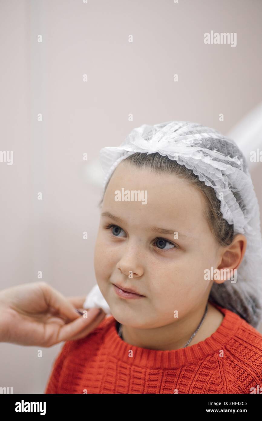 Nahaufnahme der Hände der Kosmetikerin mit antiseptischem Dekontaminationsmittel Ohren des kleinen Mädchens, Vorbereitung auf Piercing Ohren im Kosmetologie-Büro Stockfoto